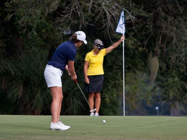 Dos jugadoras en el green de un hoyo, una atendiendo la bandera. Dos jugadoras de golf en el green de un hoyo.